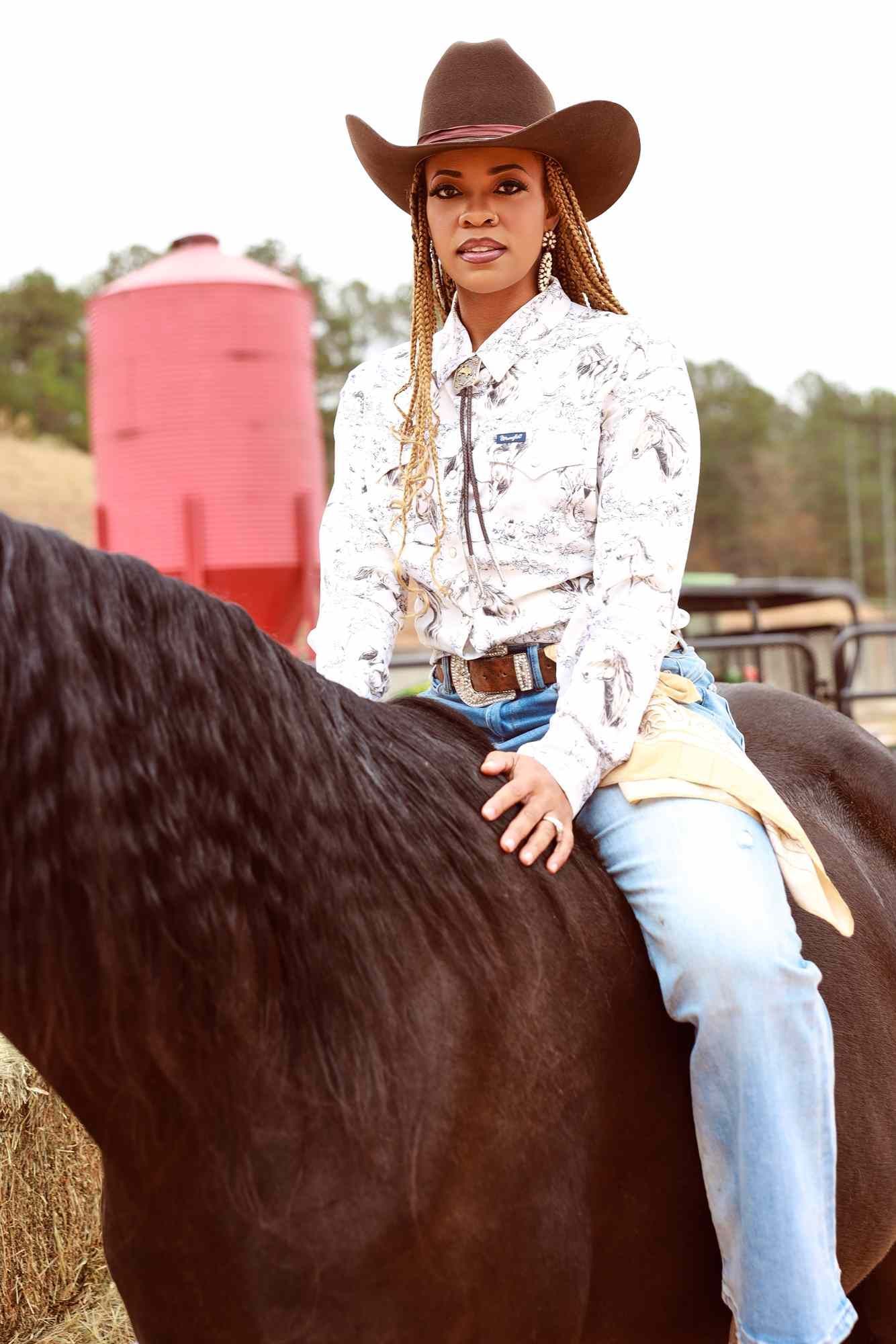 Cowgirl in a brown hat riding a dark horse at an outdoor ranch arena