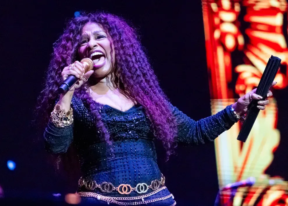 Singer performing on stage with a microphone, wearing a black outfit under purple and red lights