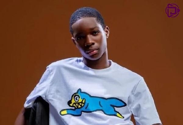 Person in a white T-shirt with a blue cartoon graphic, standing against a brown background.