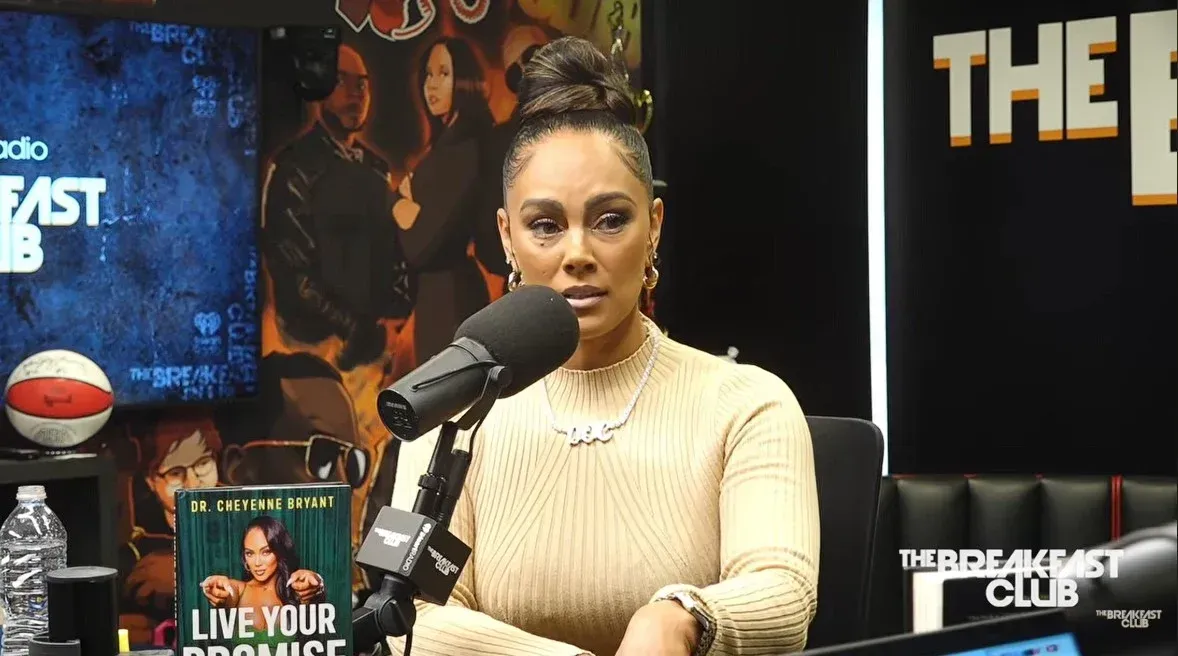 Woman speaking into a podcast microphone at a desk with books and a basketball in a studio setting