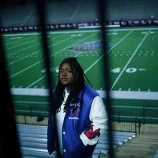 Person in a blue-and-white jacket standing in front of a football field at night