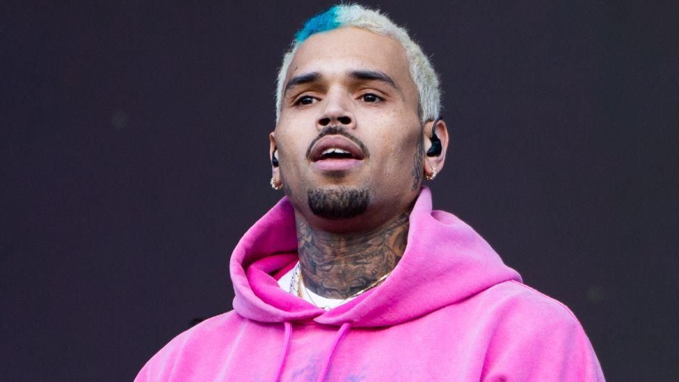 Portrait of a man with bleached hair and a pink hoodie against a dark background