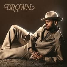 Man reclining on a brown backdrop, wearing a tan suit and hat, with “BROWN” text in the corner