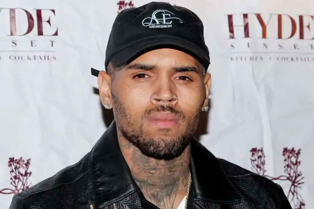 Man in black cap and leather jacket posing at a step-and-repeat event backdrop