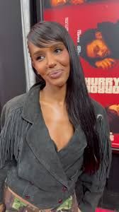 Woman in a gray jacket smiling at a movie premiere poster backdrop