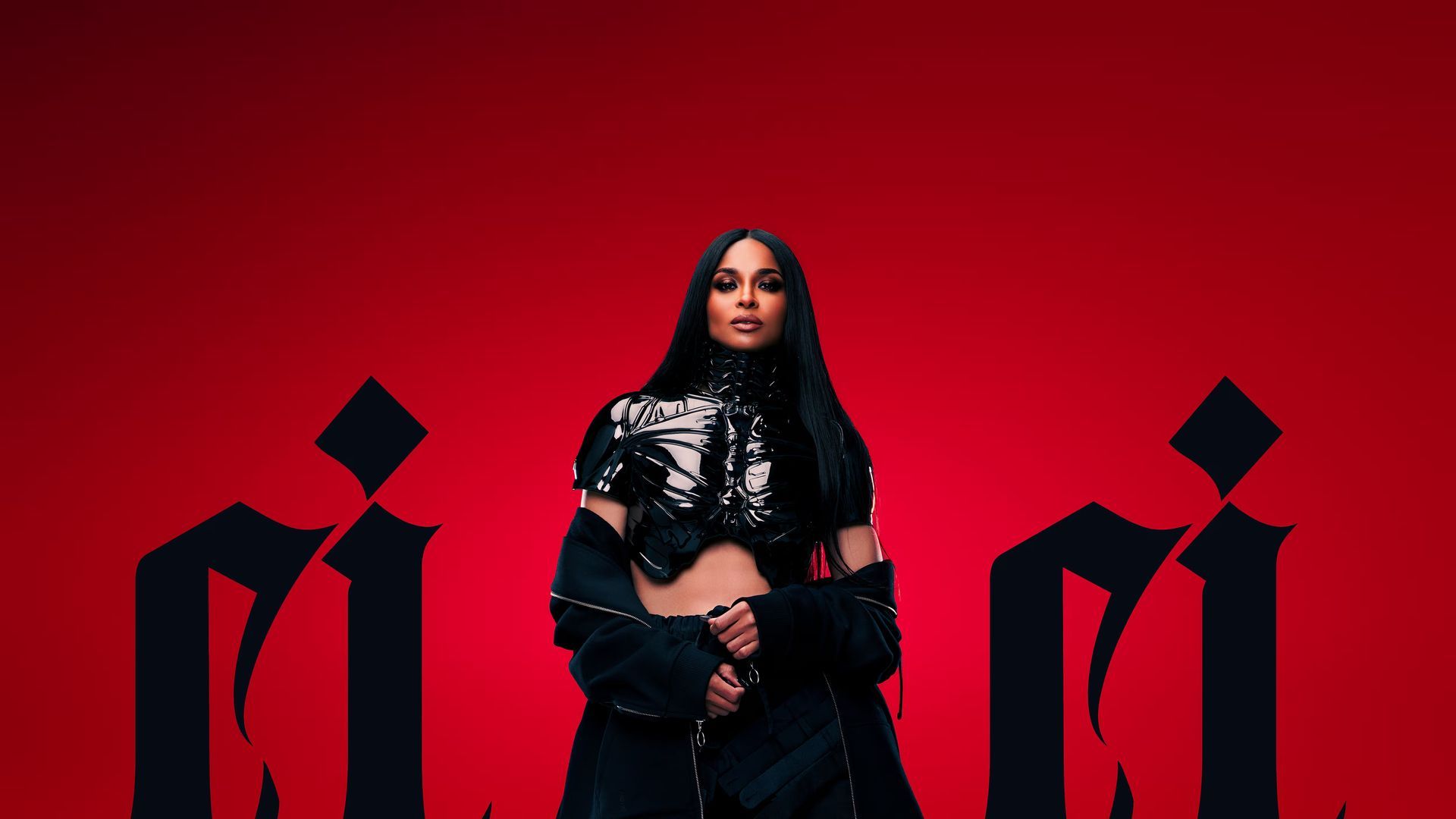 Person standing against a red background with black geometric shapes, wearing a black outfit.