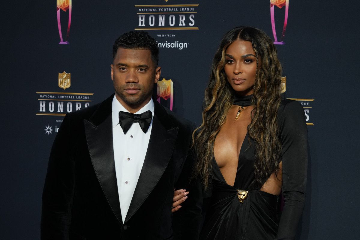 Two people in formal black attire pose on a red carpet at an honors event.