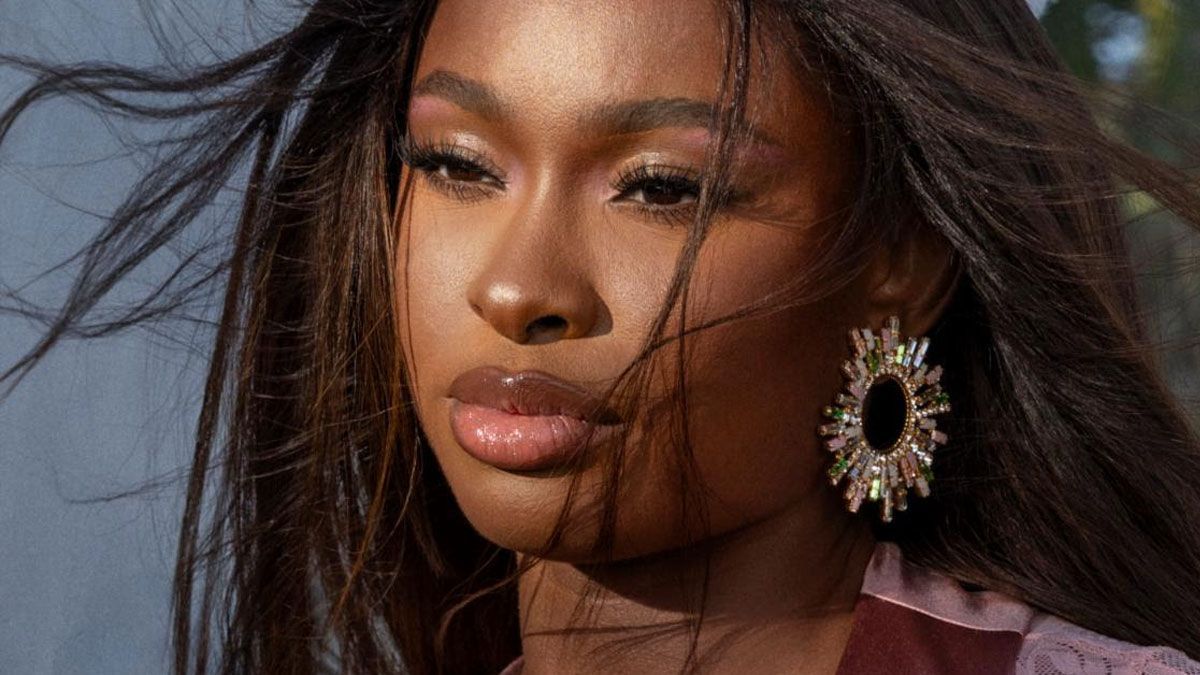 Close-up portrait of a woman with flowing hair and a large jeweled earring against a soft gray background
