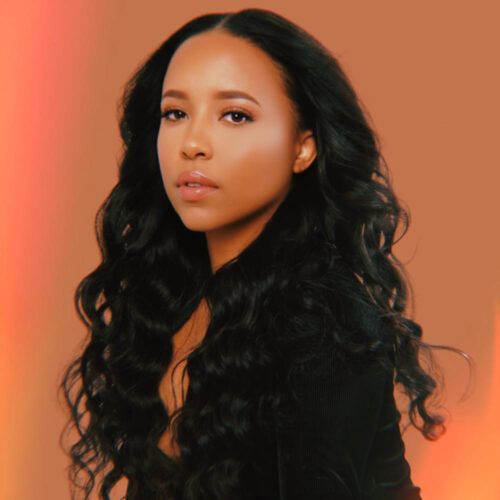 Studio portrait of a woman with long black hair against a warm orange background