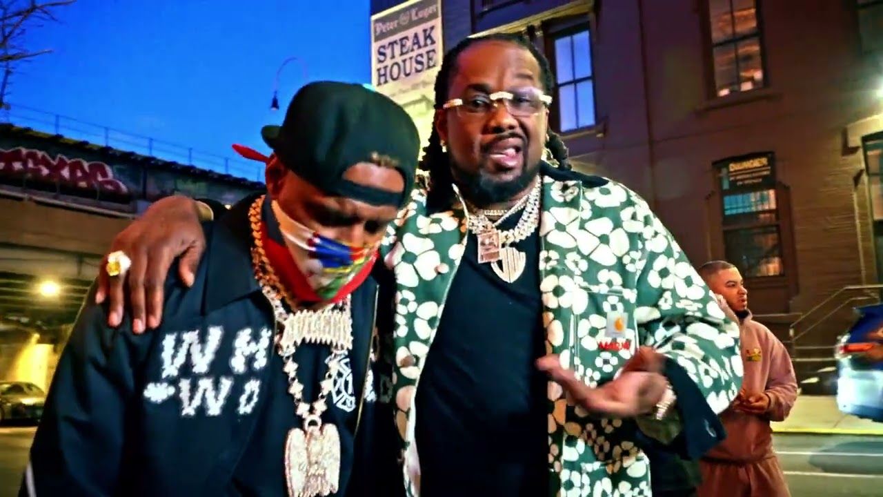 Two men posing arm-in-arm at night on a city street, one in a floral shirt, one in a black shirt and cap