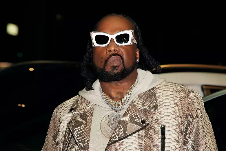Man wearing white sunglasses and a patterned jacket at night, standing in front of a car.