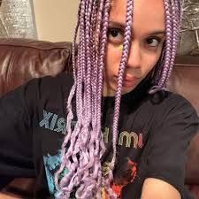 Person with long lavender braids taking a selfie on a brown leather couch, wearing a black T-shirt.