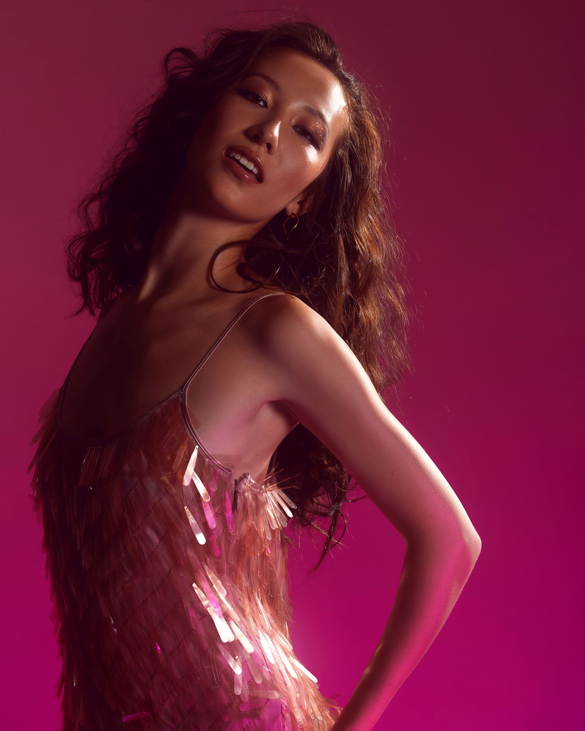 Woman in a sparkling pink dress posing against a magenta backdrop