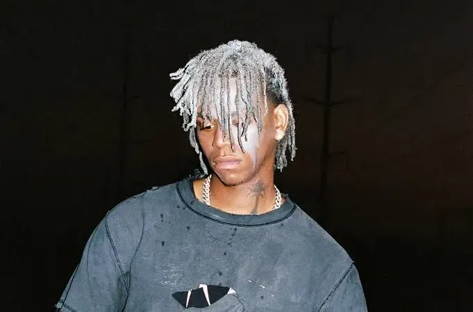 Person with silver dreadlocks and a dark shirt against a black background