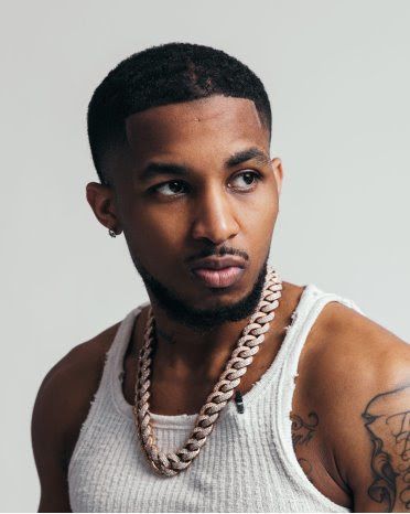 Portrait of a man in a white tank top and thick chain necklace, looking to the side against a gray background