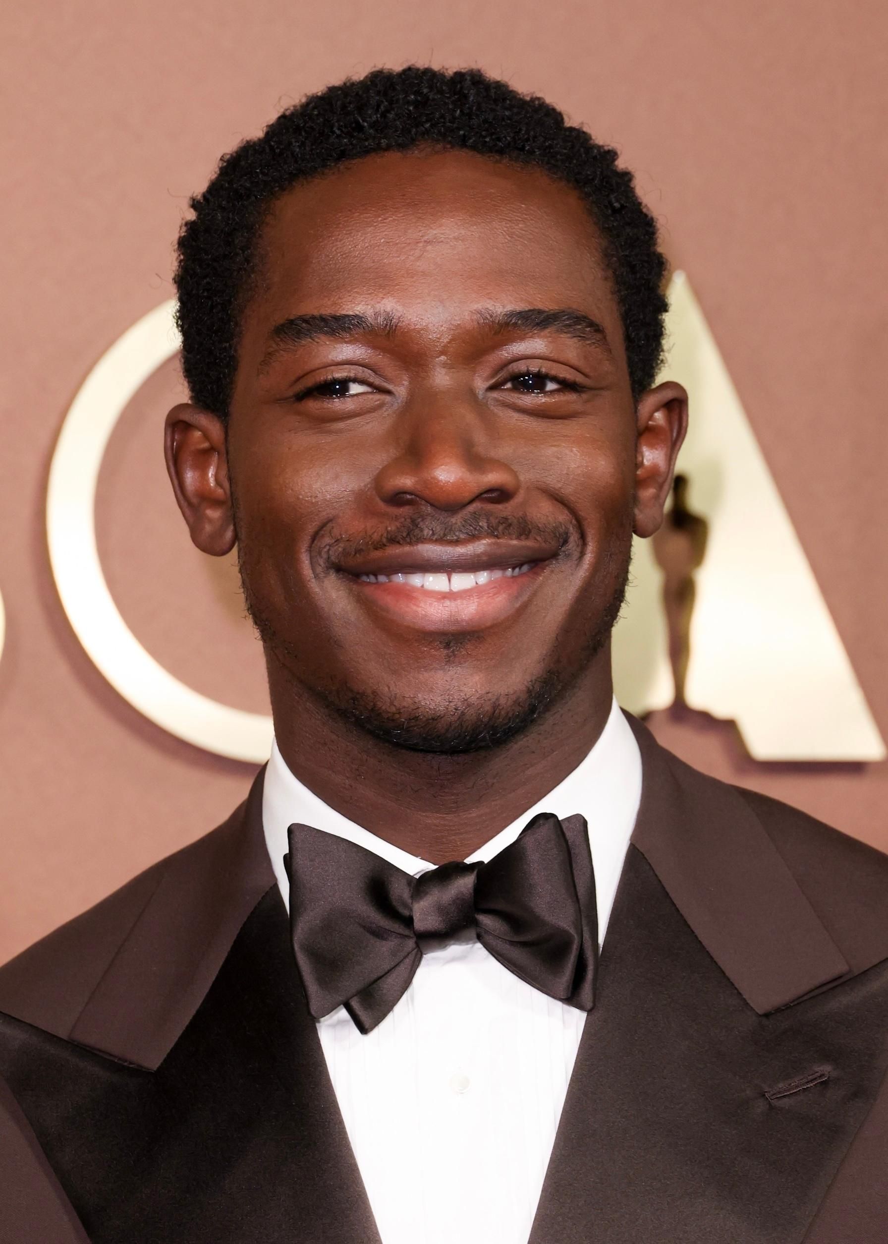 Smiling man in a black tuxedo and bow tie at a formal event backdrop