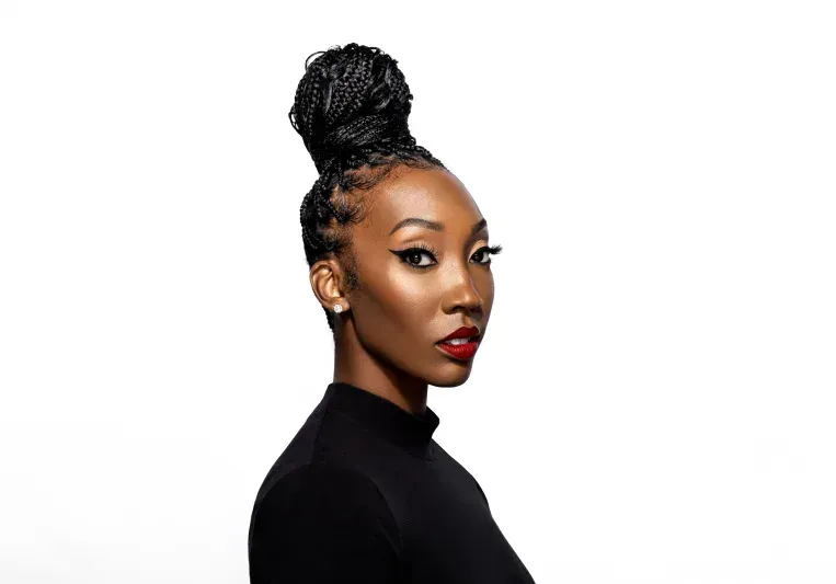 Portrait of a woman in a black top with a high braided bun against a white background