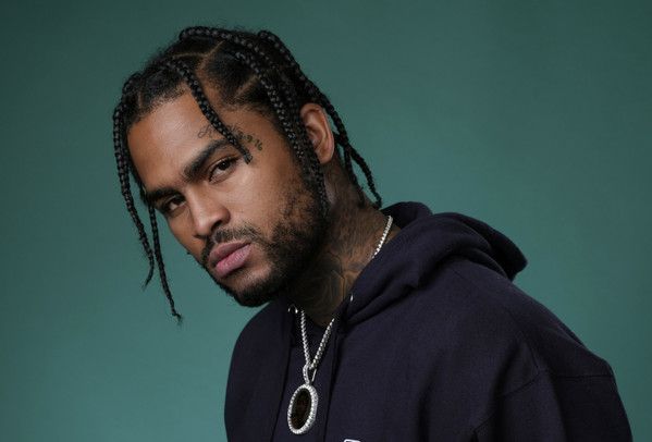 Portrait of a man with braided hair in a dark hoodie against a teal background