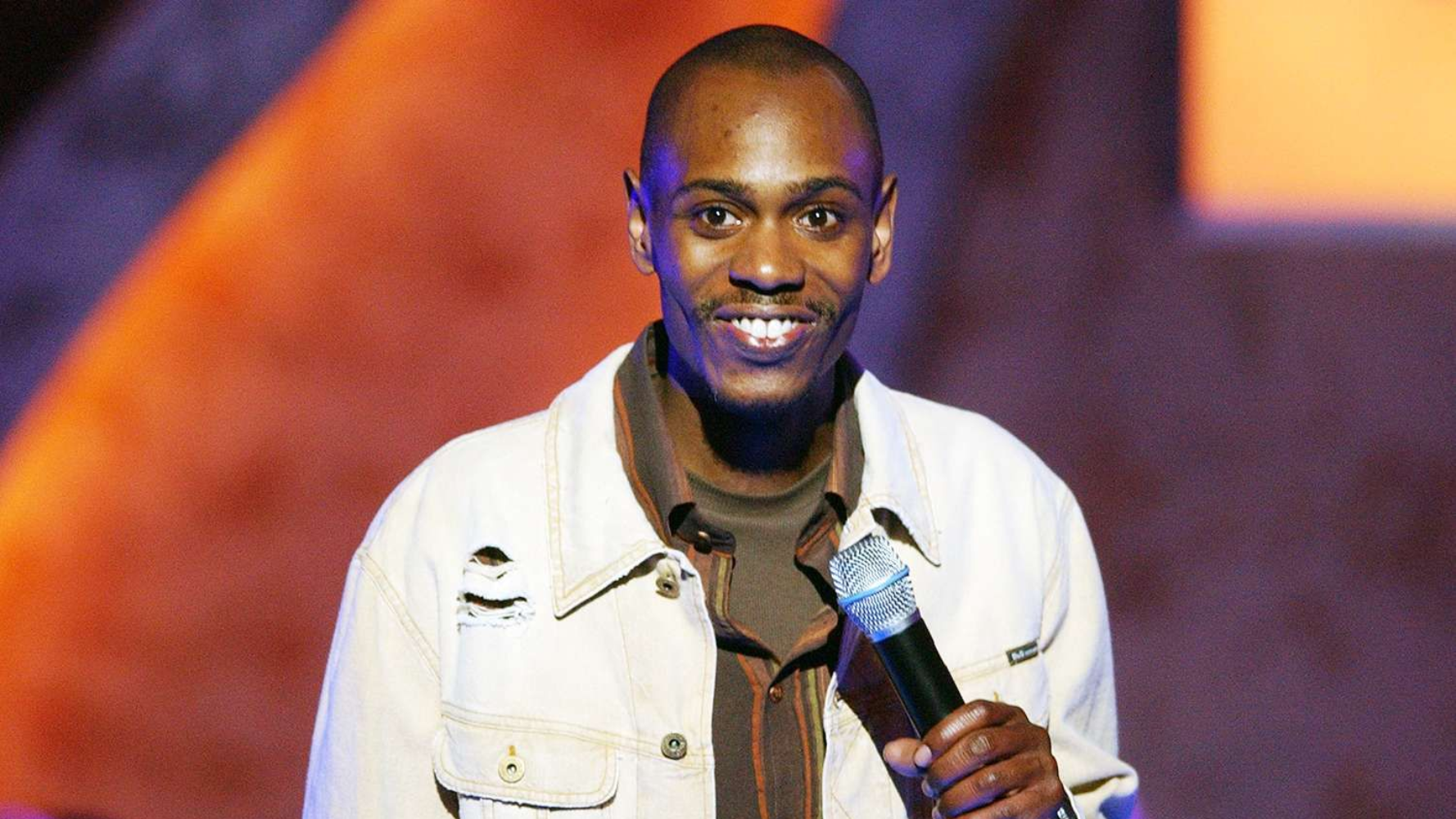 Smiling performer holding a microphone on stage with a purple and orange background