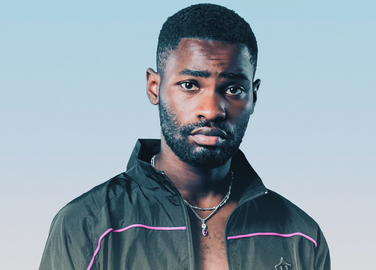 Portrait of a man in a black jacket with pink trim against a light blue background