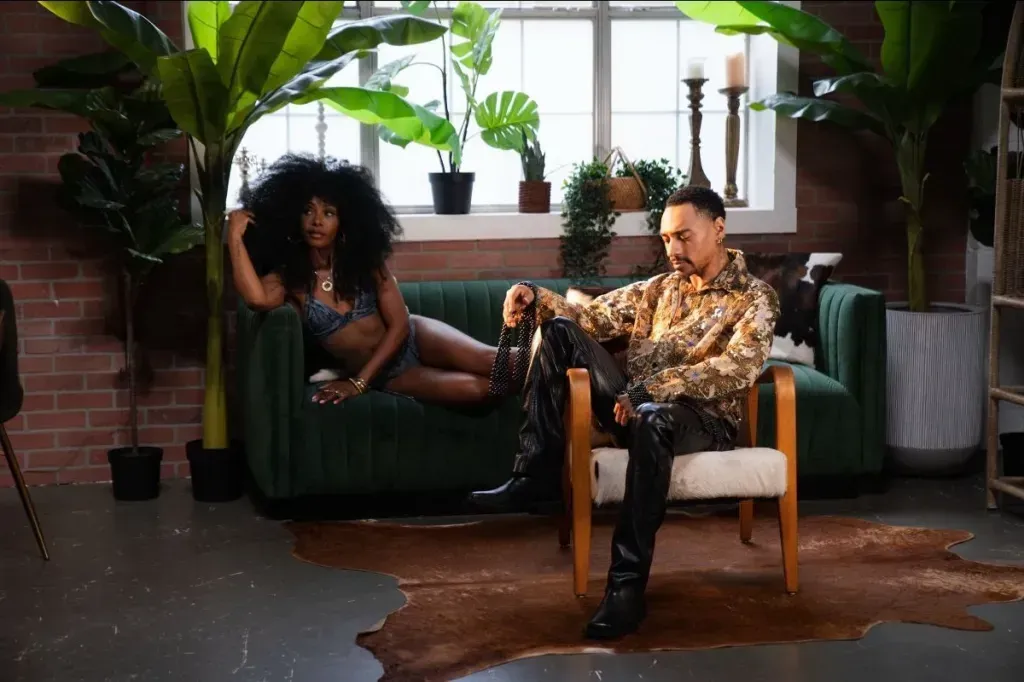 Two people lounging in a plant-filled room, one on a green couch and one in a chair, with light from a window.
