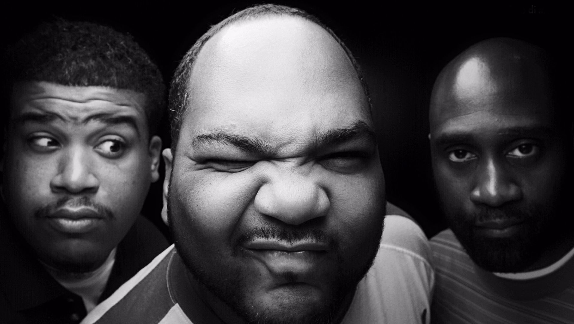 Three men in a black-and-white portrait, with the center man grimacing at the camera.