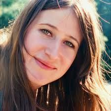 Close-up portrait of a smiling person with long brown hair in warm sunlight.