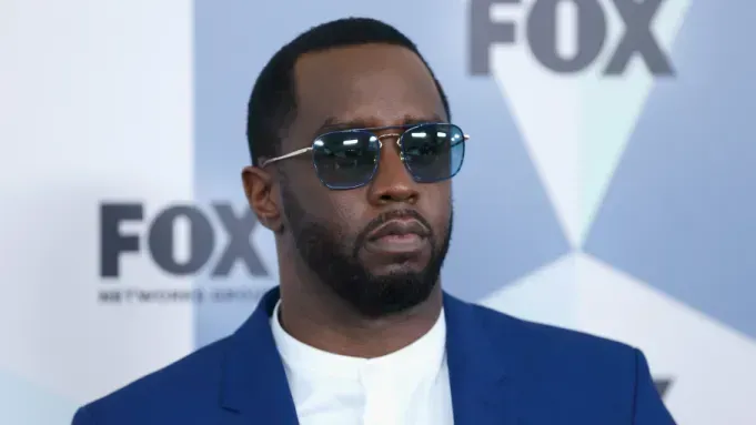 Man in sunglasses and navy blazer at a FOX event backdrop