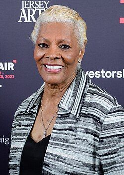 Smiling woman with short silver hair at a Jersey Arts event, wearing a black-and-white striped jacket.