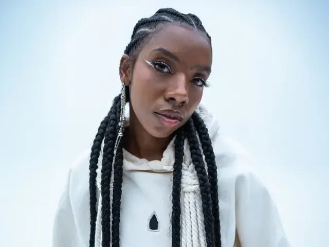 Person with braided hair wearing a white hoodie against a light background