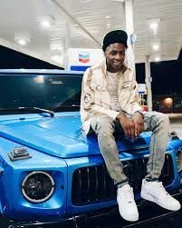 Man sitting on the front of a blue SUV at a gas station at night, smiling at the camera