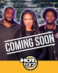 Three people behind “COMING SOON” text with HOT 97 logo on a yellow banner.