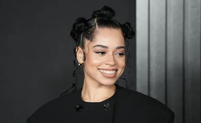 Smiling person in a black outfit against a dark gray background