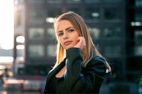 Woman in a black coat looking at the camera outdoors in a city setting