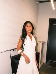 Woman in a white dress posing indoors beside a wall and staircase.