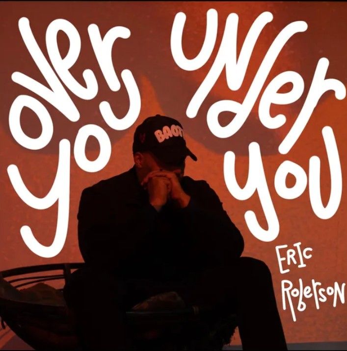 Person in black sitting against a red background with large white text reading “over you,” by Eric Roberson