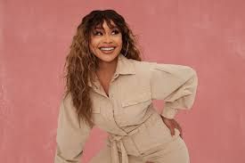 Smiling woman in a beige outfit posing against a pink background
