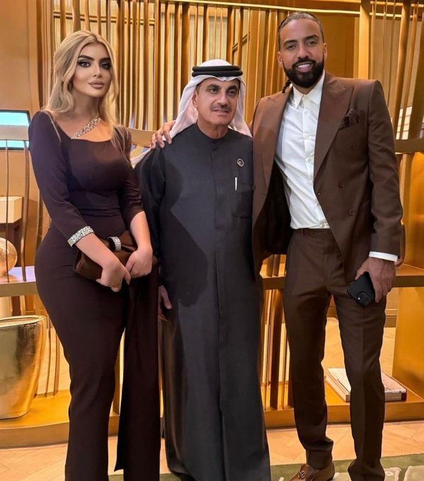 Three people posing indoors in formal attire, with gold-toned decor behind them.