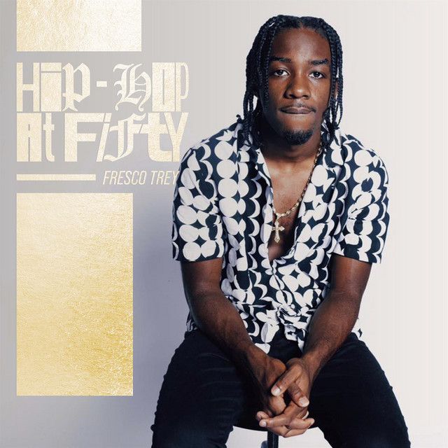Portrait of a seated man in a black-and-white patterned shirt with “Hip-Hop at Fifty” text on the left.