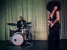 Singer in a black dress with a drummer on a stage in front of green curtains