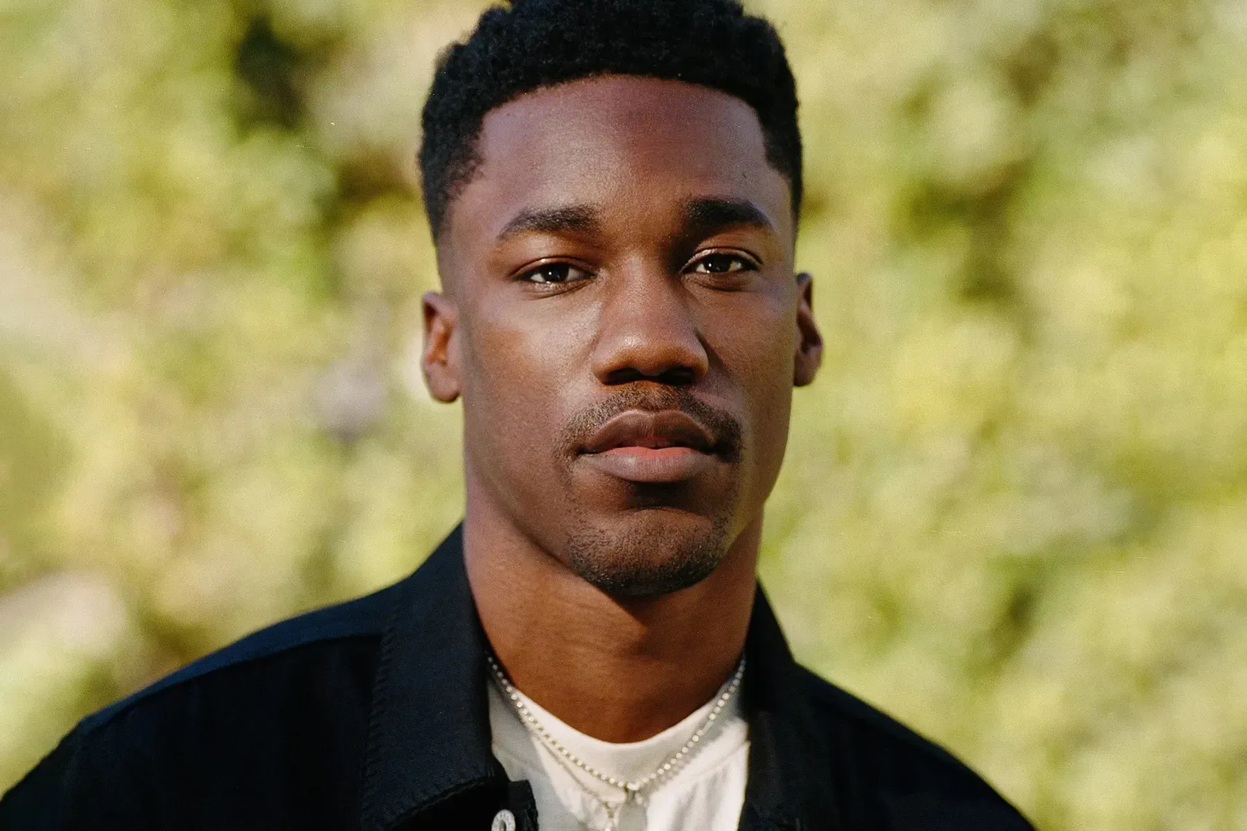 Portrait of a man in a dark jacket and white shirt against a blurred outdoor background