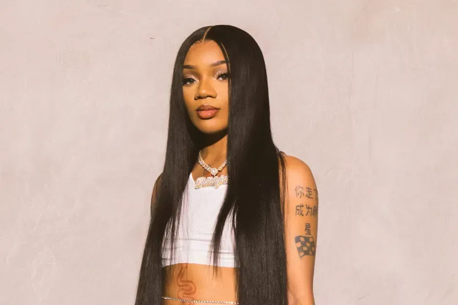 Portrait of a woman with long straight hair, wearing a white crop top against a plain beige background