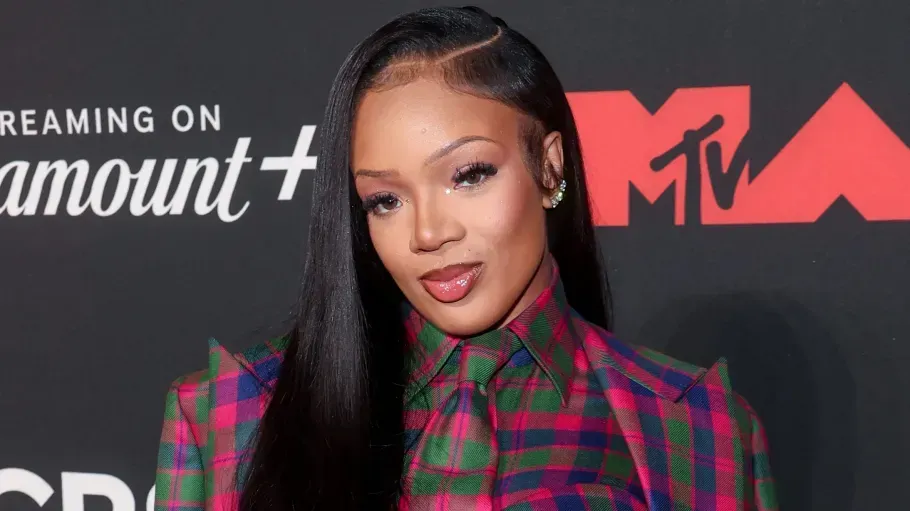 Woman with long straight hair at an MTV event, wearing a red-and-green plaid outfit, posing on the red carpet