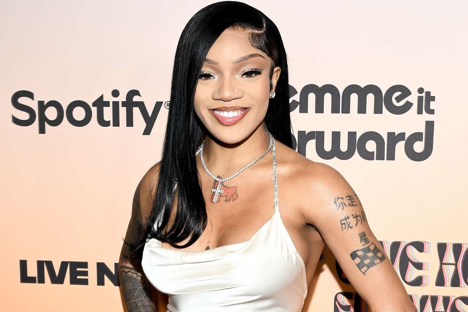 Woman in a white dress smiling at a Spotify event backdrop.