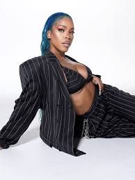 Person in a black pinstripe suit reclining on a white background, with blue hair and a confident pose