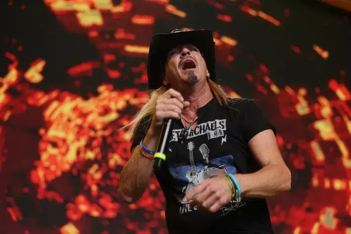 Singer in black shirt and cowboy hat performing on stage with fiery red background