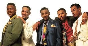 Five men posing together against a white backdrop, wearing colorful jackets and looking at the camera.