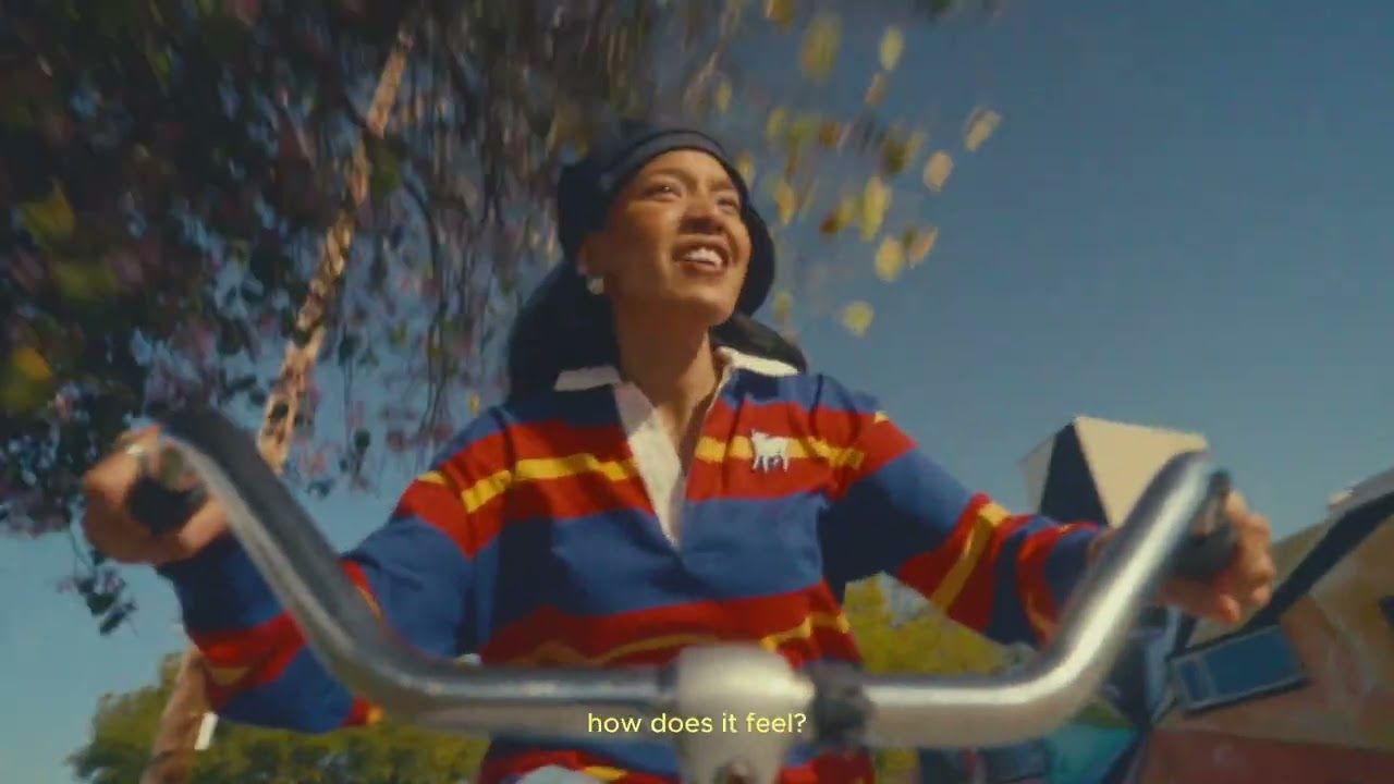 Smiling person riding a bicycle under falling leaves, wearing a colorful striped shirt.