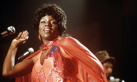 Singer in a sparkling red dress and cape performing on stage with microphones under warm lights
