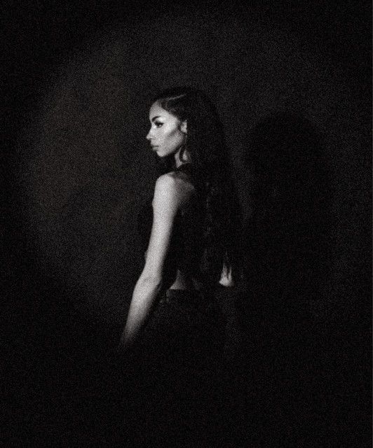 Monochrome portrait of a woman in profile against a dark background, looking over her shoulder.